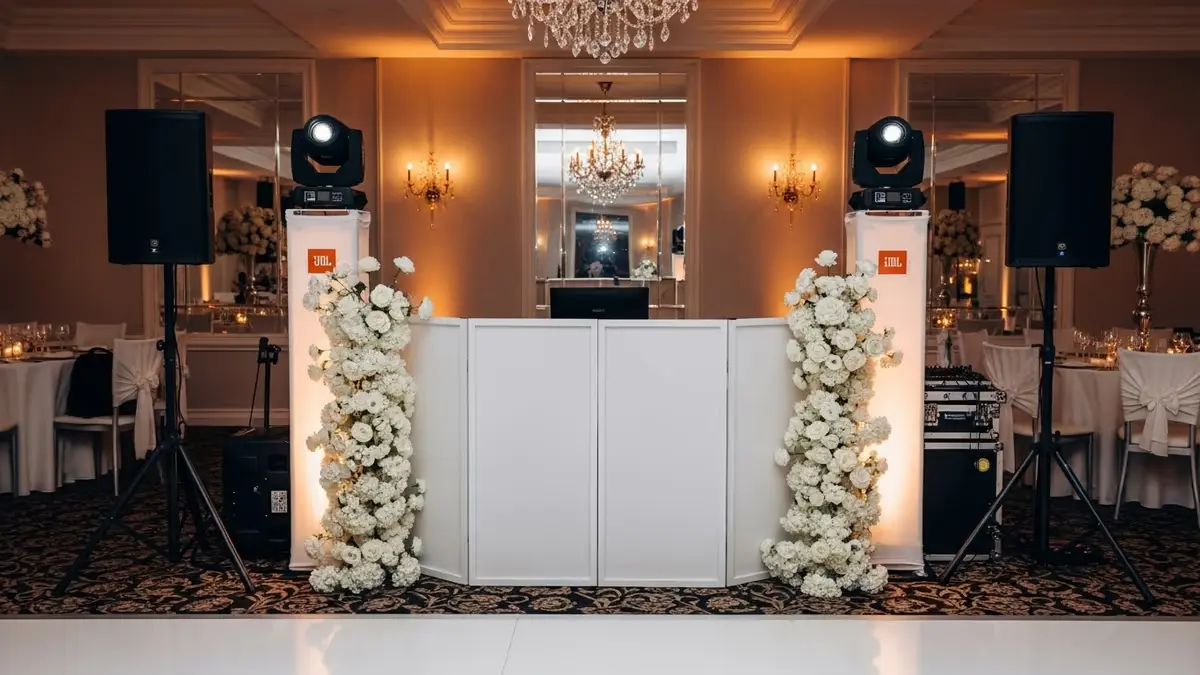 Cabina de DJ blanca con bocinas JBL, cabezas móviles y arreglos florales en un salón de bodas