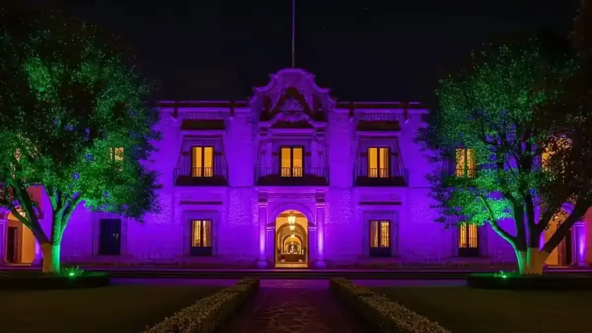 Fachada de hacienda bañada en luz violeta con árboles iluminados en verde durante una boda nocturna