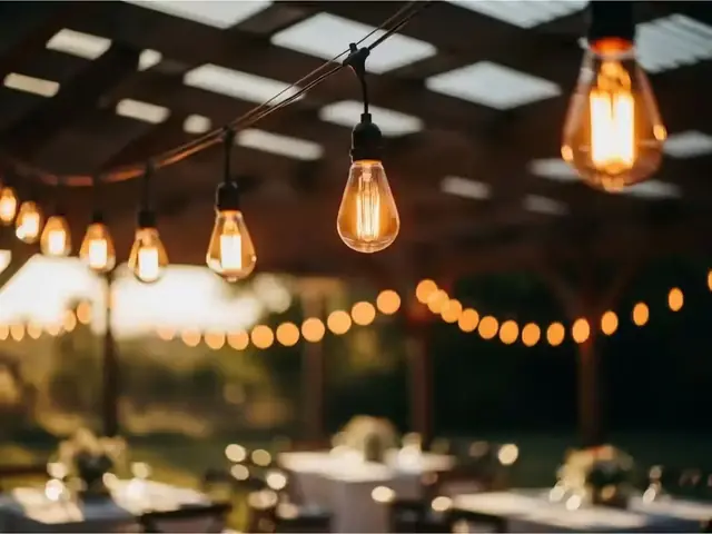 Guirnaldas de focos Edison colgadas de una pérgola sobre mesas de recepción al atardecer