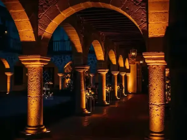 Arcos coloniales de cantera iluminados con luz ámbar desde la base de cada columna