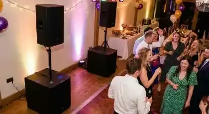 Bocina y subwoofer en una fiesta con invitados bailando bajo luces de colores