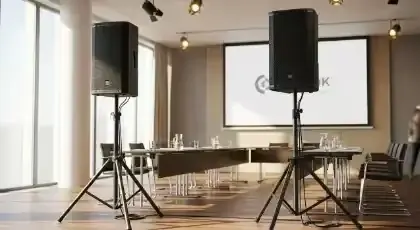 Bocinas sobre tripié a los lados de una pantalla de proyección en una sala de conferencias