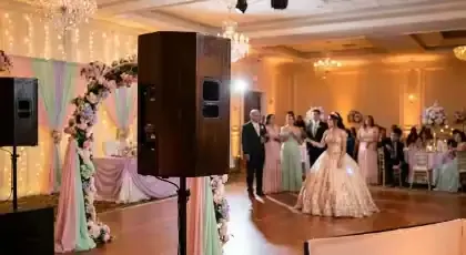 Bocina profesional sobre tripié en un salón de XV años con arco floral y quinceañera en la pista