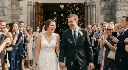 Novios saliendo de la ceremonia entre burbujas con invitados a los lados