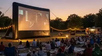 Pantalla inflable gigante con proyección al aire libre frente a público sentado en el pasto al atardecer